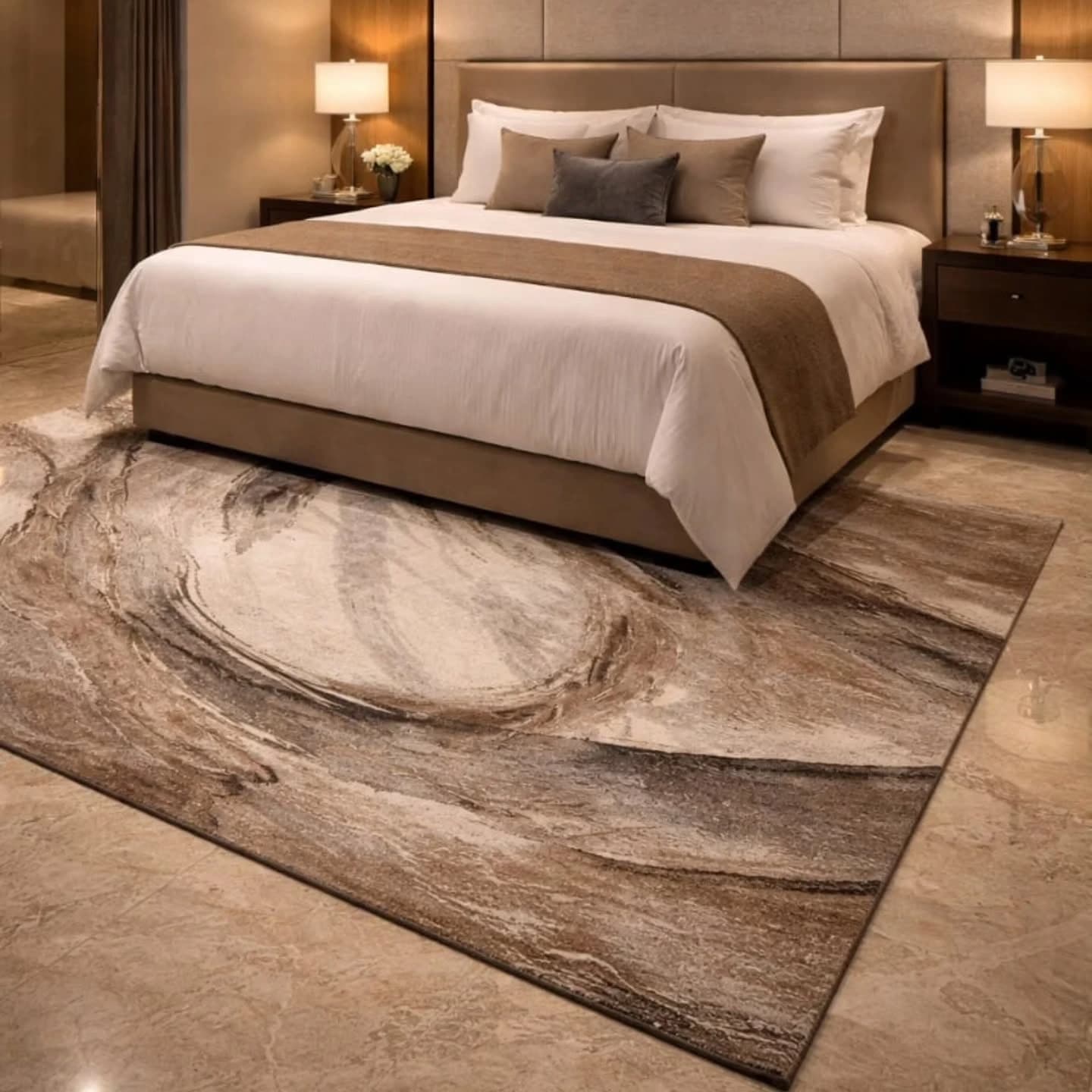 A large rug with a swirling brown and cream marbled pattern laid on stone flooring in front of a king bed with a padded headboard, white linens and matching bedside lamps.
