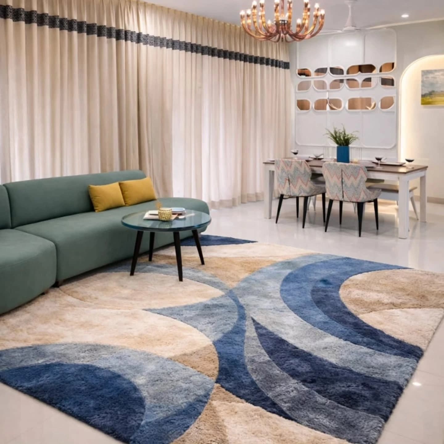 An open-plan living and dining area with a green sectional sofa, glass coffee table and a large blue and beige patterned shag rug, with a dining table and copper chandelier beyond.