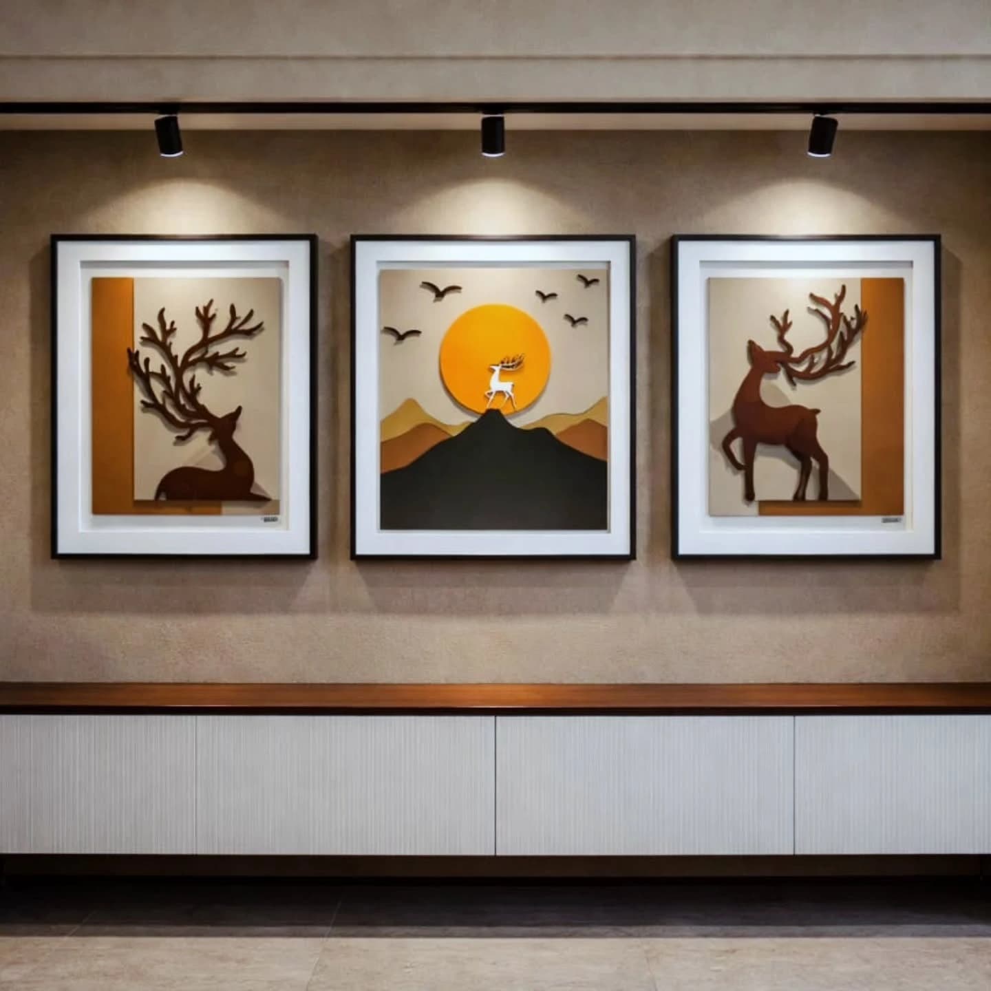 Three framed three-dimensional deer artworks in black frames lit by track spotlights above a white ribbed sideboard.