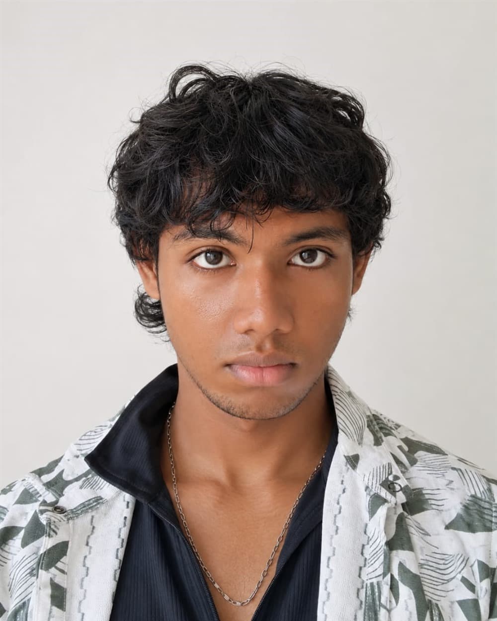 Chaitanya Gaikwad, founder of XIYÀTO, in a head-and-shoulders portrait facing the camera, wearing an open patterned shirt over a dark collared top against a plain pale wall.